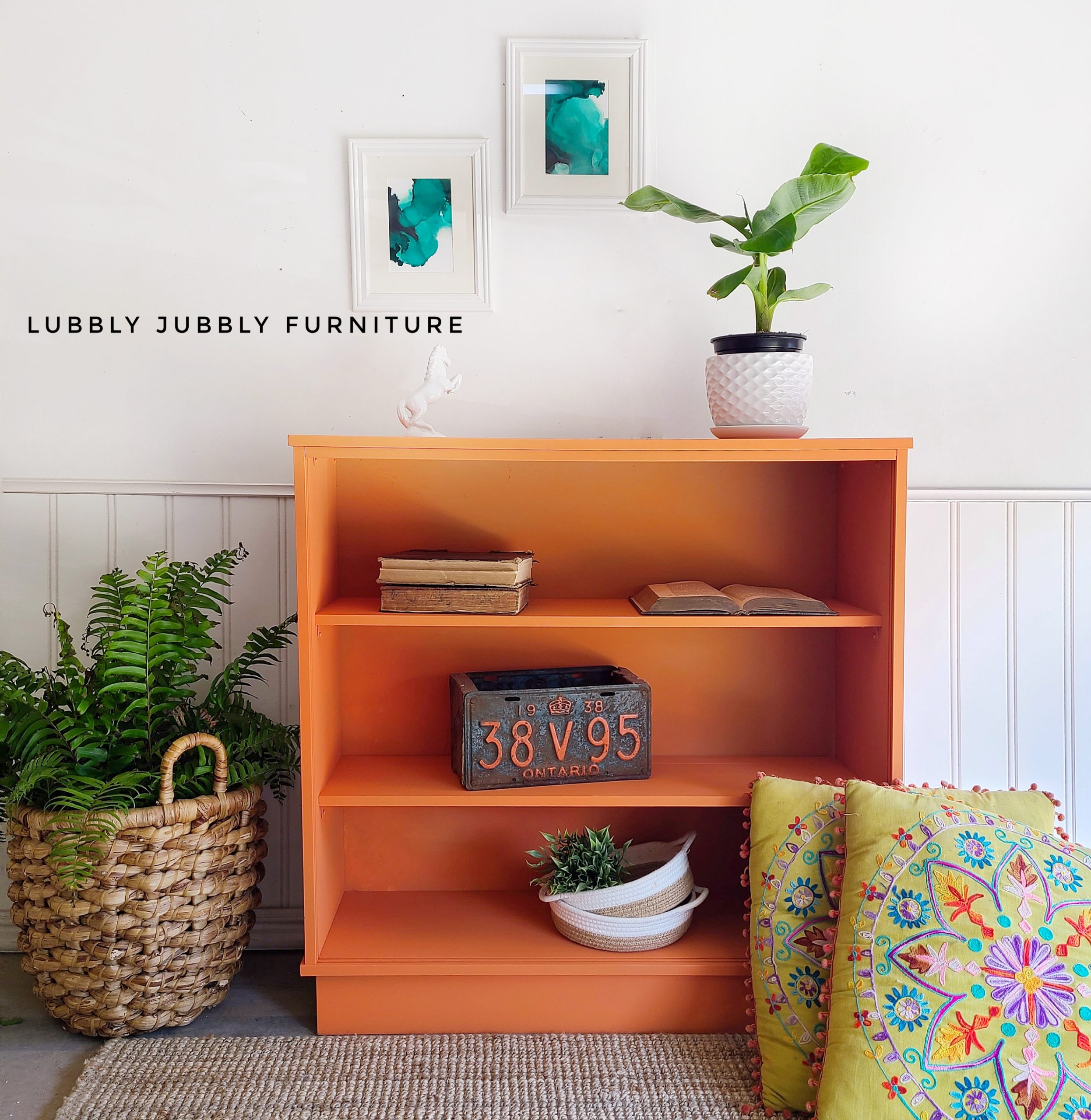 three shelf bookcase in bold, citrus orange with wicker basket, pillow, license plate, books